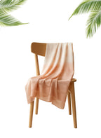 Light pink towel draped over a wooden chair with palm leaves in the background